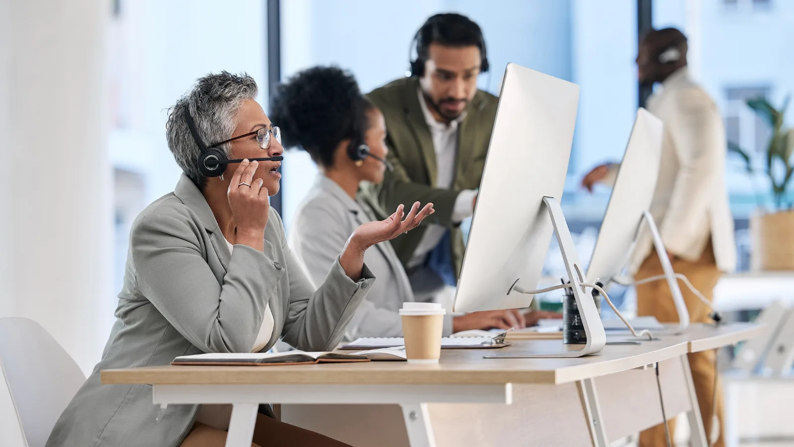 Equipe de atendimento de provedor de internet trabalhando em computadores com headsets em escritório operacional.